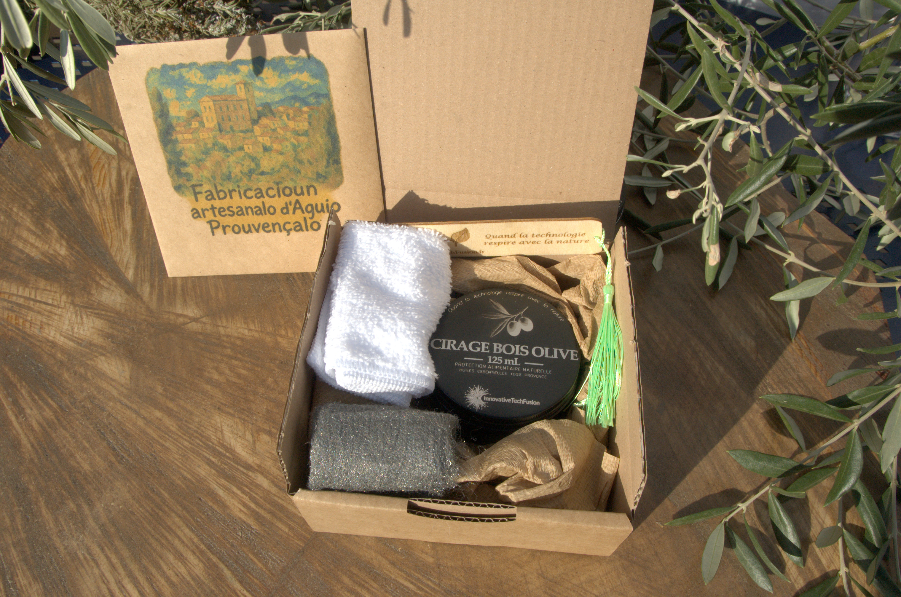 Boîte cadeau en carton brun ouverte dévoilant le kit cirage : pot, accessoires et carte disposés dans du papier de calage